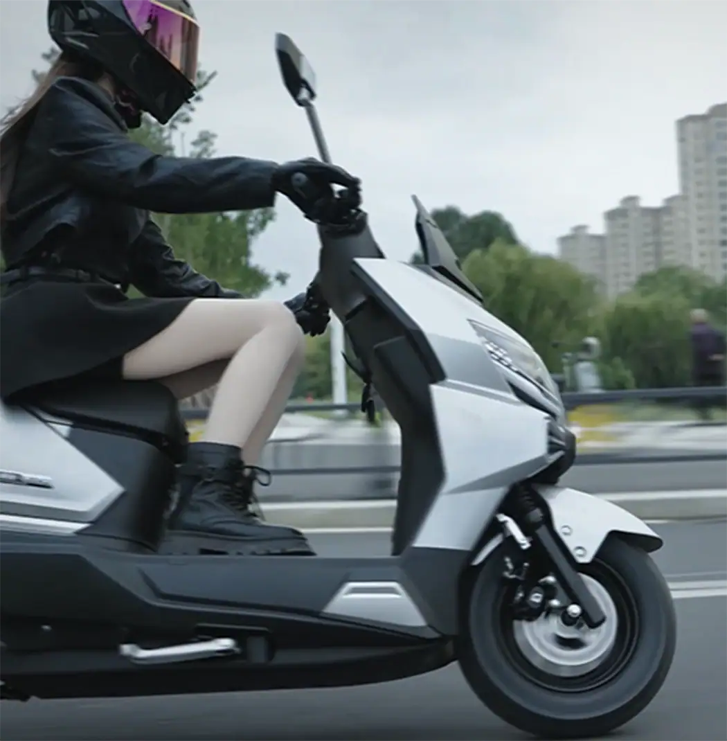 产品/场景电动滑板车 wearing a helmet and 时尚 outfit, commuting through an urban area with high-rise buildings in the background.